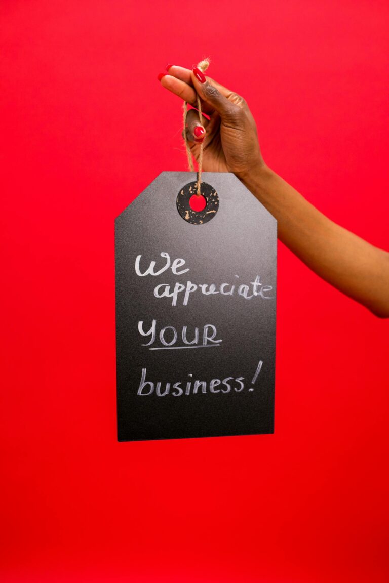 A hand holding a 'We appreciate your business' sign on a bold red background, conveying gratitude.