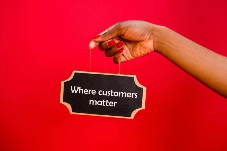 A sign with 'Where customers matter' held by a hand against a vibrant red background.